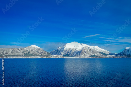Amazing landscape of outdoor view of coastal scenes of huge mountain covered with snow on Hurtigruten voyage during a blue sky