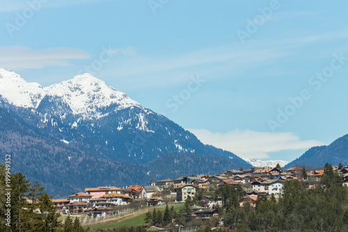 Picturesque view on the village with high mountain peaks covered in snow on the background, Dolomites, Trentino, Italy