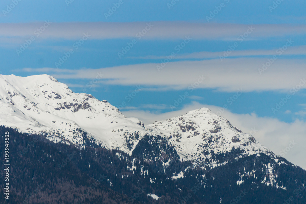 Picturesque view of the high mountain peaks covered in snow with white clouds on the blue sky on the background, Dolomites, Trentino, Italy