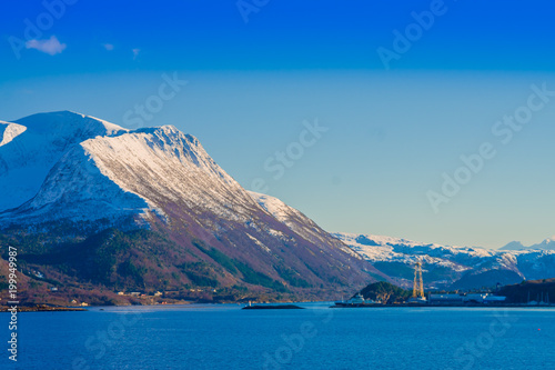 Outdoor view of mountain range in Norway. The beautiful mountain partial covered with snow in Hurtigruten region with some buildings in the horizont in Norway