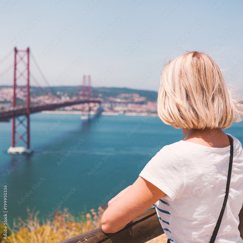 Female traveler standing next to the statue of National Sanctuary of Christ the King and enjoys panoramic views of Lisbon and the bridge of April 25.