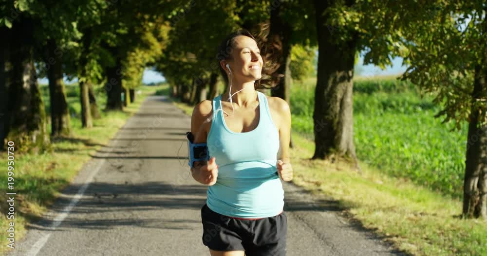 a happy girl fit relaxed jogging and running in a street with trees and nature, using headphones for music and run slow in sunset. concept of happiness for sports and fitness relaxation in nature a happy girl fit relaxed jogging and running in a street with trees and nature, using headphones for music and run slow in sunset. concept of happiness for sports and fitness relaxation in nature