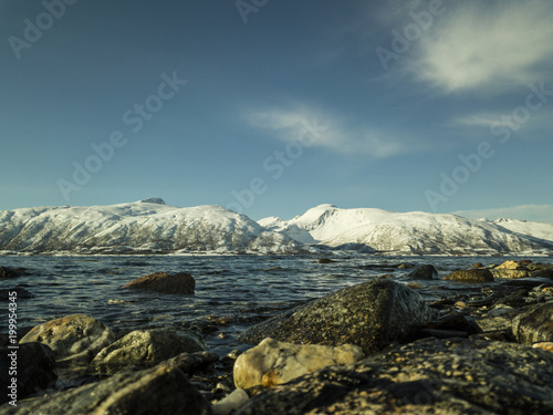 Rocks on the shore with snowy mountains in the background