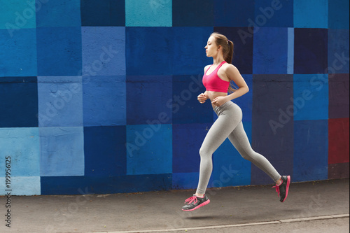 Side view of woman running against bright wall photo