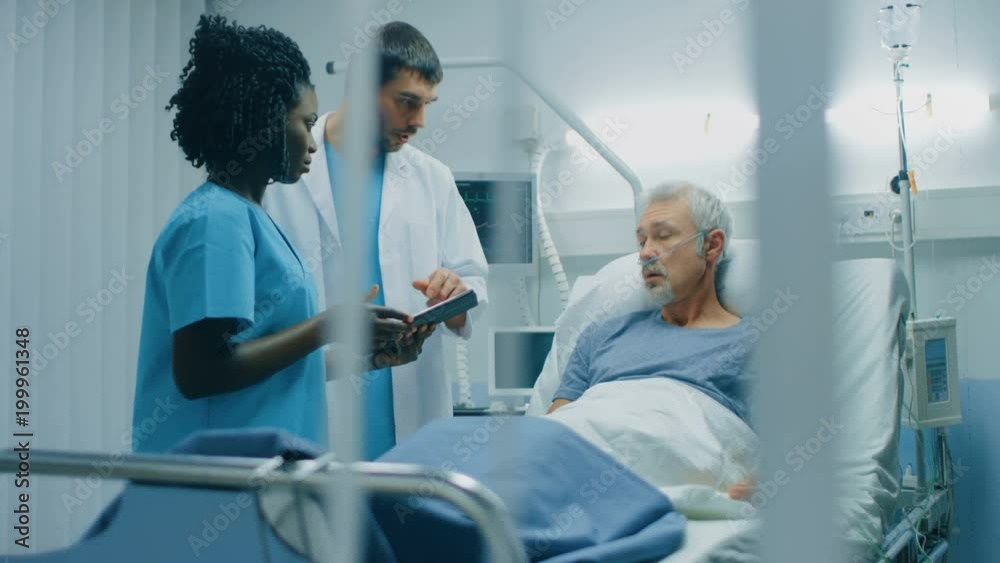 In the Hospital, Senior Man Lying in the Bed, Talks with Doctor and Nurse who Use Tablet Computer. Technology Helps Cure Patients, Modern Hospital Ward. Shot on RED EPIC-W 8K Helium Cinema Camera. In the Hospital, Senior Man Lying in the Bed, Talks with Doctor and Nurse who Use Tablet Computer. Technology Helps Cure Patients, Modern Hospital Ward. Shot on RED EPIC-W 8K Helium Cinema Camera.