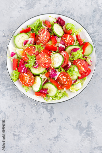 Fresh vegetable salad with tomatoes, cucumbers, sweet pepper and sesame seeds. Vegetable salad on white plate