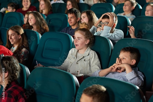 Sideview of laughing children watching movie in the cinema hall. Kids look funny, happy and satisfied. Boys and girls wearing colorful clothes with different prints and smiling.