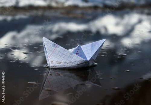 children's paper boat made from a school notebook in mathematics swims in the early spring puddle