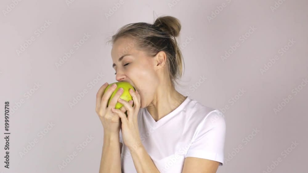 Attractive young girl bites a big green apple. She lifts her thumb up and smiles Attractive young girl bites a big green apple. She lifts her thumb up and smiles