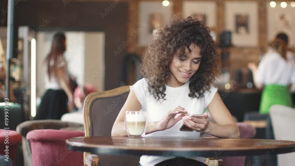 beautiful hispanic woman messaging on smartphone and smiling sincerely. young girl drinks coffee in a cafe beautiful hispanic woman messaging on smartphone and smiling sincerely. young girl drinks coffee in a cafe