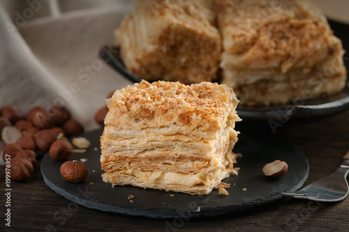 Slices of sweet classic layered cake Napoleon, fork and hazelnuts 