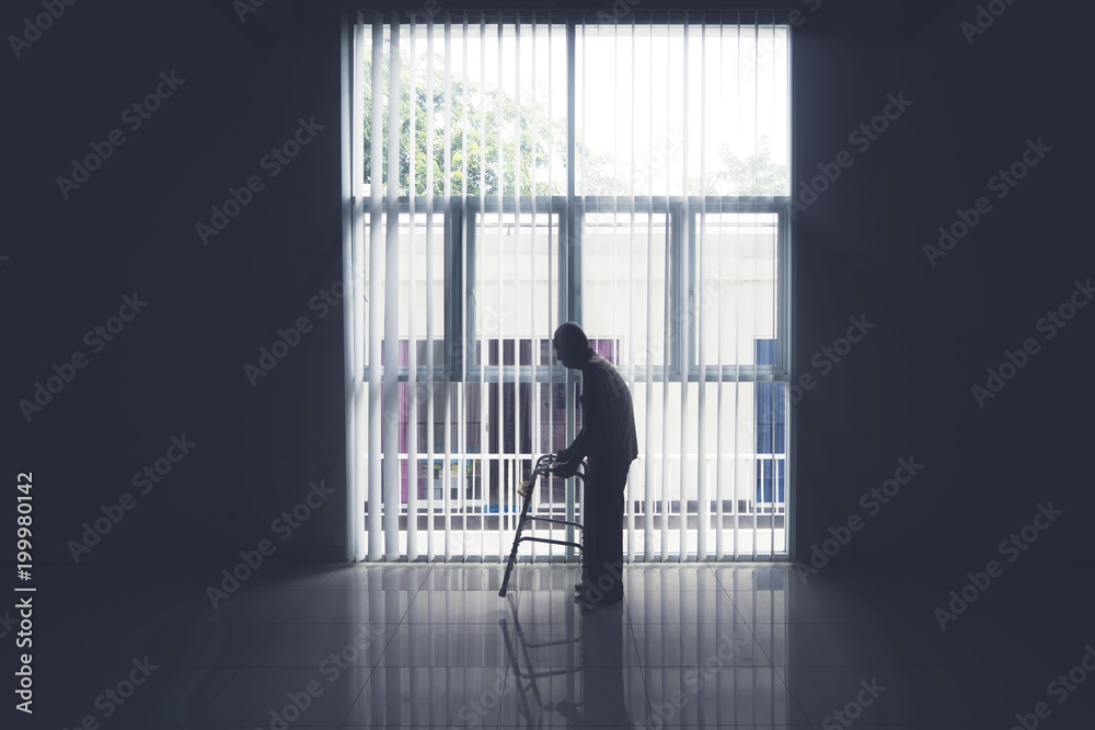 Old man walks near the window with a walker