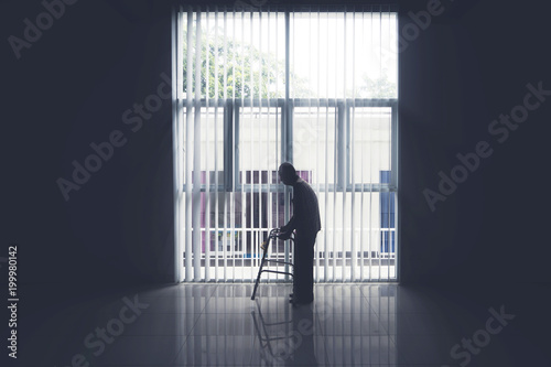 Old man walks near the window with a walker