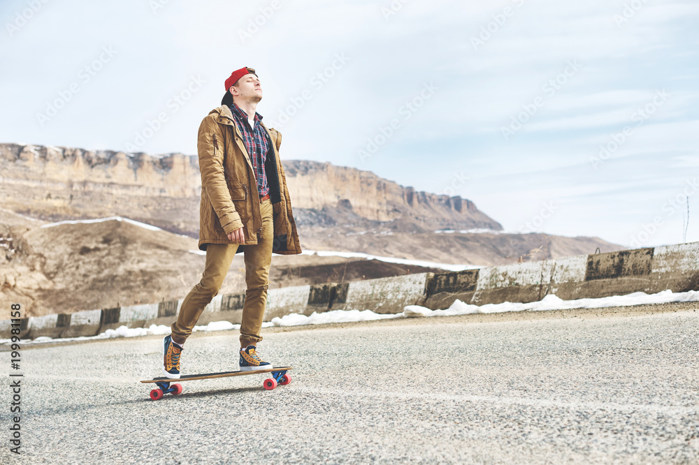 Stylish happy Young guy in a cap and trousers joggers rolling down a  mountain road on a longboard, enjoying life Stock Photo | Adobe Stock