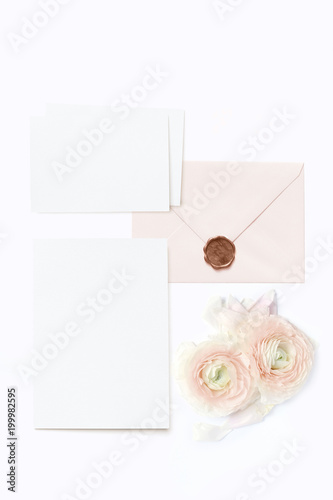 Feminine wedding, birthday desktop mock-ups. Blank greeting cards, envelope with seal and pink Persian buttercup flowers. White table background. Flat lay, top view.