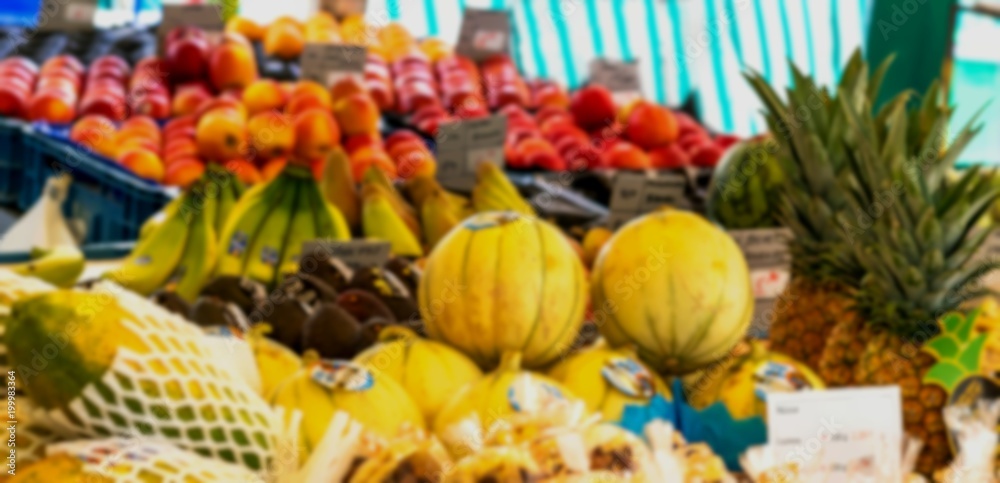 Blurred view of melon, papaya, pineapple, apples, bananas at city fruit and vegetable market.