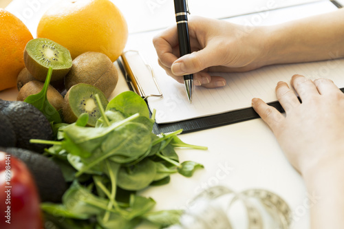 Fototapeta Naklejka Na Ścianę i Meble -  Nutritionist woman writing diet plan on table full of fruits and vegetables