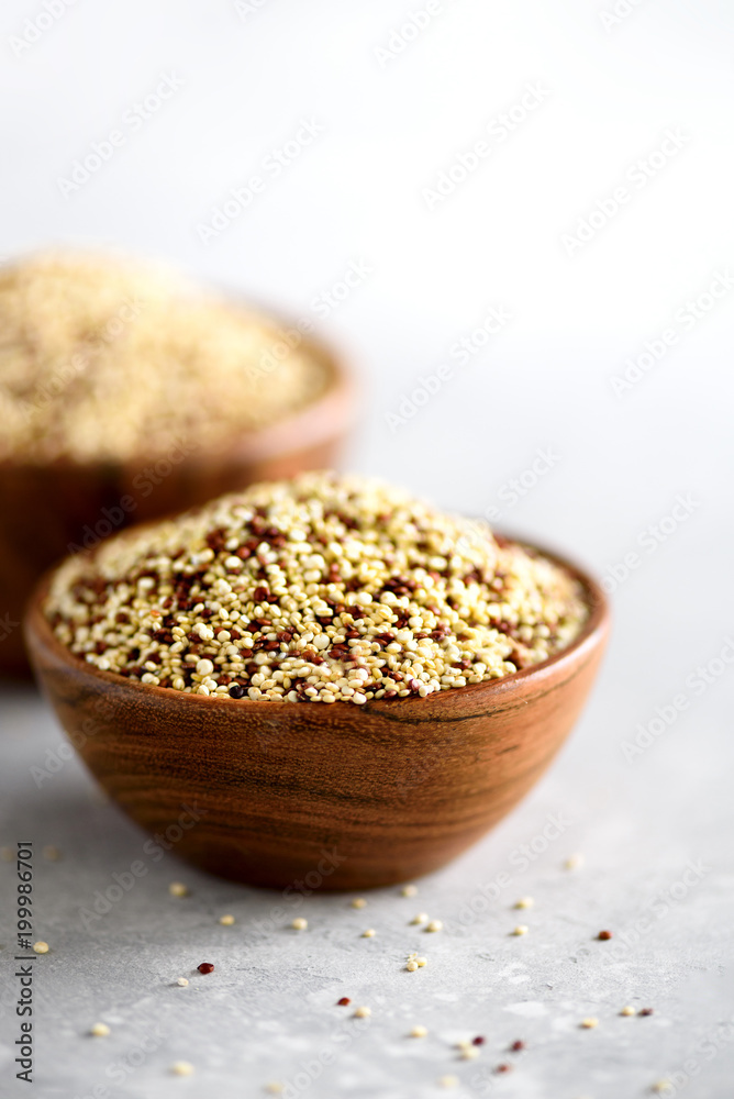 White and red raw organic quinoa in wooden bowl and rosemary on grey background. Healthy food ingredients. Copy space White and red raw organic quinoa in wooden bowl and rosemary on grey background. Healthy food ingredients. Copy space