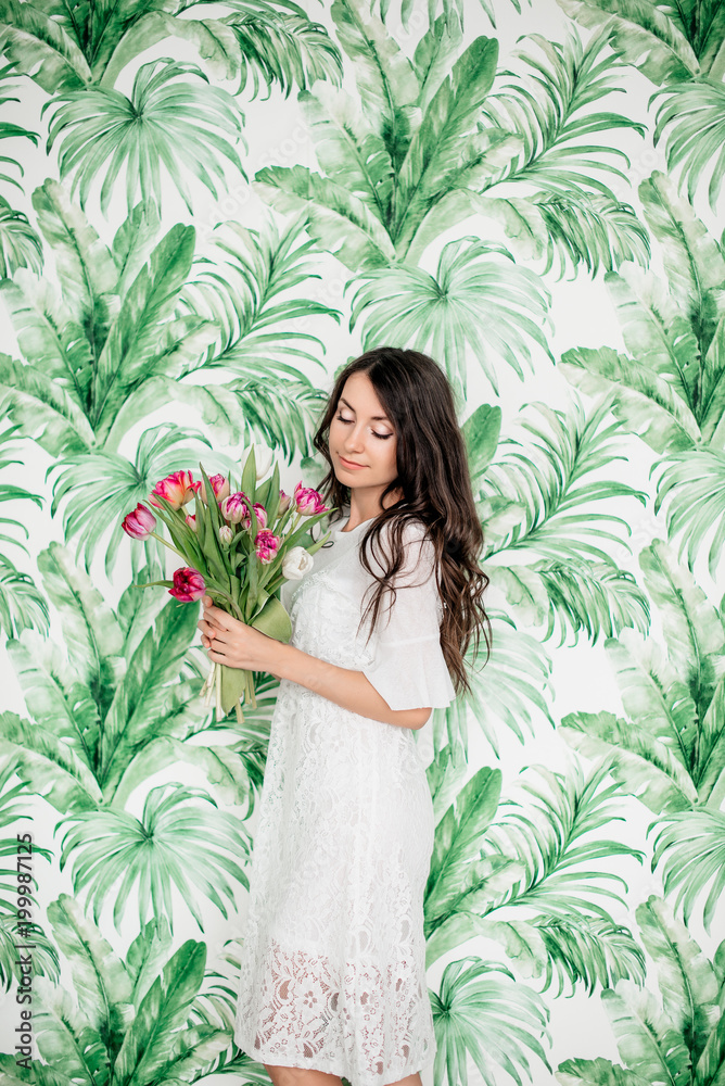 beautiful young girl with dark hair is standing in a white short dress and is holding a bouquet of tulips in her hand beautiful young girl with dark hair is standing in a white short dress and is holding a bouquet of tulips in her hand
