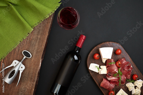 Above overhead view flat lay still life of assortment various cheese and delicatessen and red wine on a old wooden board on black table photo
