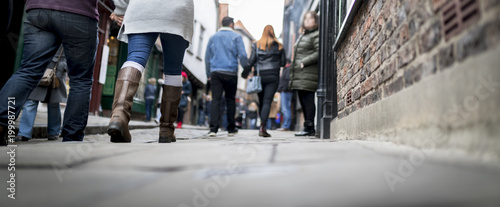 Low down shot of people and couple walking holding hands down a old traditional cobbled English street whilst browsing in shops on retail therapy day