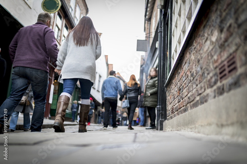 Low down shot of people and couple walking holding hands down a old traditional cobbled English street whilst browsing in shops on retail therapy day photo