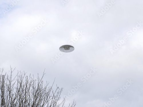 UFO Sighting, flying saucer in the cloudy sky over trees, reflective metal aircraft