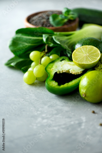 Organic green vegetables and fruits on grey background. Copy space, flat lay, top view. Green apple, zucchini, cucumber, avocado, kale, lime, kiwi, grapes, banana, broccoli, marbled lentils, mung bean