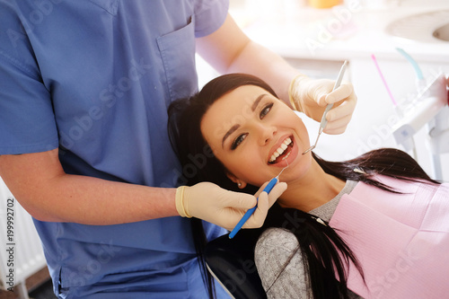 Dentist in blue uniform and white gloves cares on a sexy brunette caucasian woman, stand behind her.