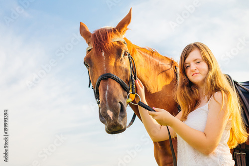 A pretty girl holds a horse for a bridle and they look in the camera lens © Ivan
