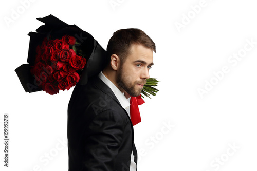 A young man in a suit with a big bouquet of roses on his shoulder. 