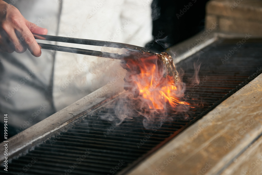 Chef grilling beef steak on flame on bbq in the kitchen of restaurant, close-up Chef grilling beef steak on flame on bbq in the kitchen of restaurant, close-up