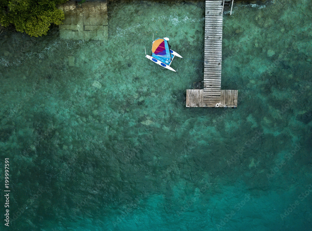 Catamaran, wooden pier and blue water from above