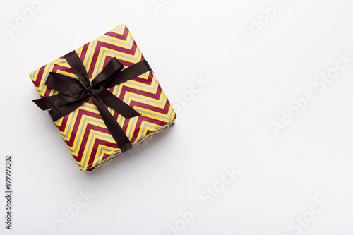 Hands holding wrapped gift box with colored ribbon as a present for Christmas, new year, mother's day, anniversary, birthday, party,  on white background, top view. Present for a colleague at work.