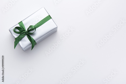 Hands holding wrapped gift box with colored ribbon as a present for Christmas, new year, mother's day, anniversary, birthday, party,  on white background, top view. Present for a colleague at work.