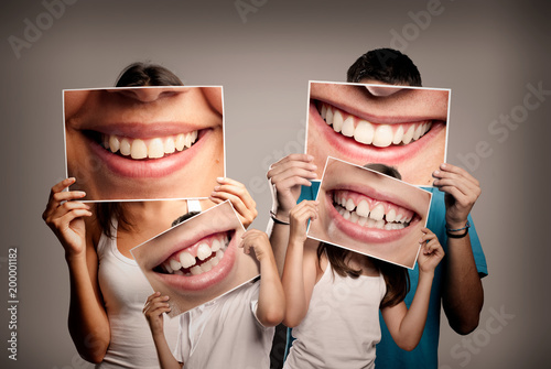 Fototapeta Naklejka Na Ścianę i Meble -  young family with children holding a picture of a mouth smiling on a gray background
