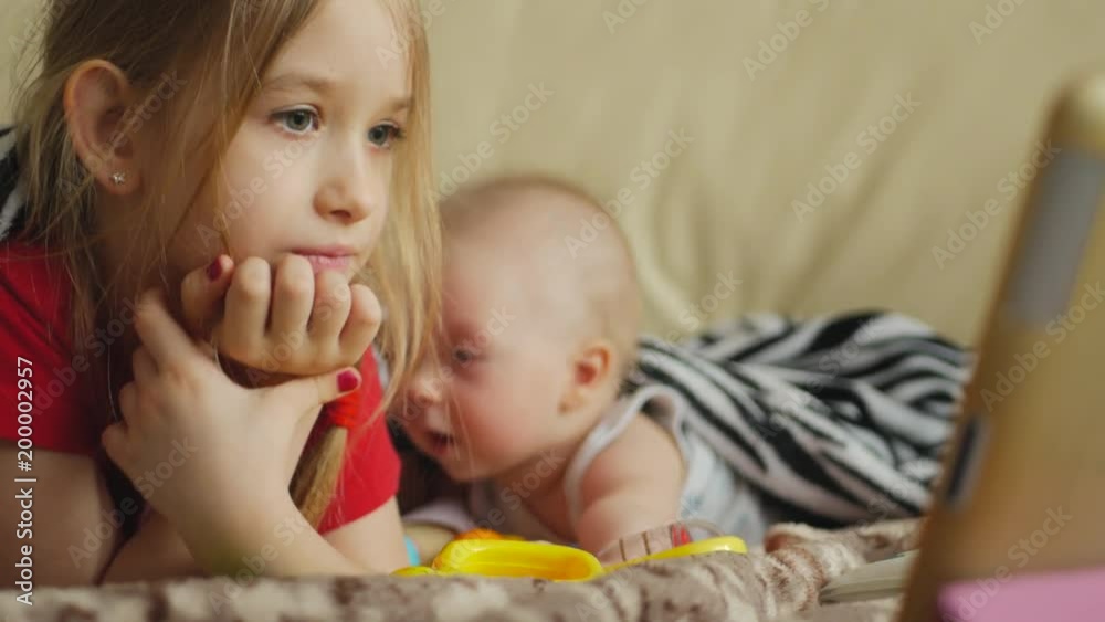 Lovely brother and sister lying in sofa at home. Concept of Brother And Sister Together Forever. Watching the tablet computer. Lovely brother and sister lying in sofa at home. Concept of Brother And Sister Together Forever. Watching the tablet computer.