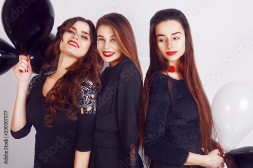 Crazy party time of three beautiful stylish women in elegant evening casual black dress celebrating , having fun, dancing on white background. Best friends girls with black and white balloon .