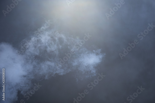 Blue-grey cloud of smoke emerges from bottom left over a hazy black background