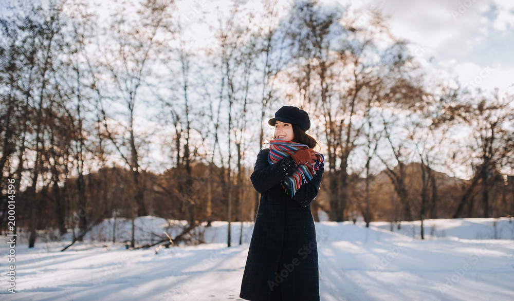 A beauty young caucasian girl in a coat is wrapped in a warm scarf. Winter forest with snow. Warm clothes.