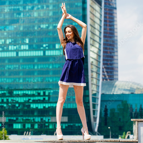 Young woman in a blue dress is stretching near skyscrapers