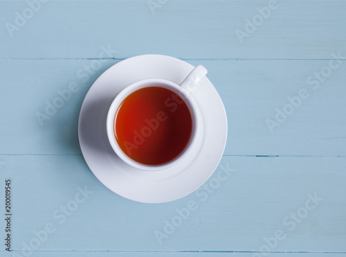 A cup of tea stands on the blue painted boards. View from above. A white cup and a white saucer.
