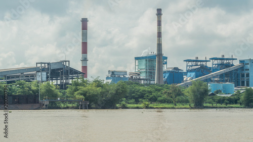 coal power plant on riverbank with barge full of coal in the dock. Indonesia