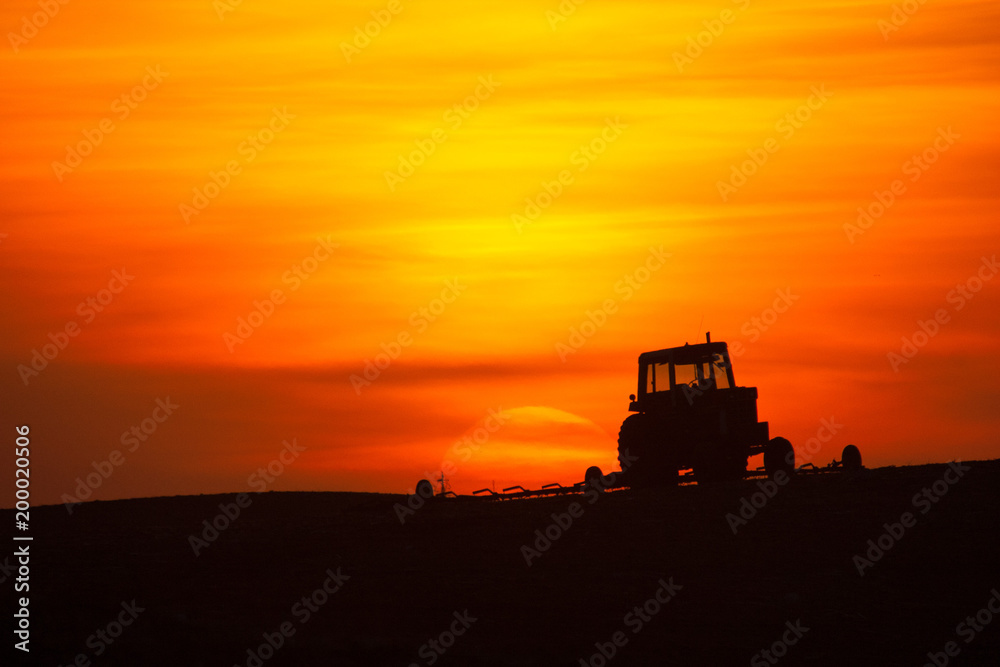 Fototapeta premium Tractor and cultivator silhouetted at sunrise