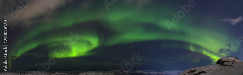Aurora and clouds in the night sky in winter over the tundra and hills. © Moroshka
