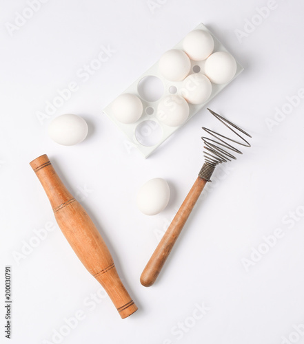 The cooking process. Plastic tray with white eggs, rolling pin, whisk on a white background. Top view..