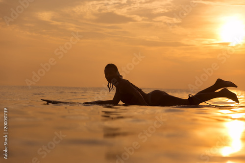 Surfer girl in ocean at sunset time