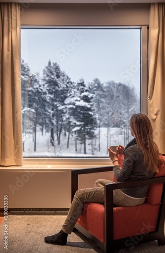 Girl sitting and drinking coffee in front of winter window