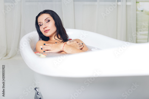 Beautiful young sexy girl with dark hair wet, natural makeup, takes bath with milk tan perfect skin in romantic atmosphere, beauty cosmetic salon and spa for woman.