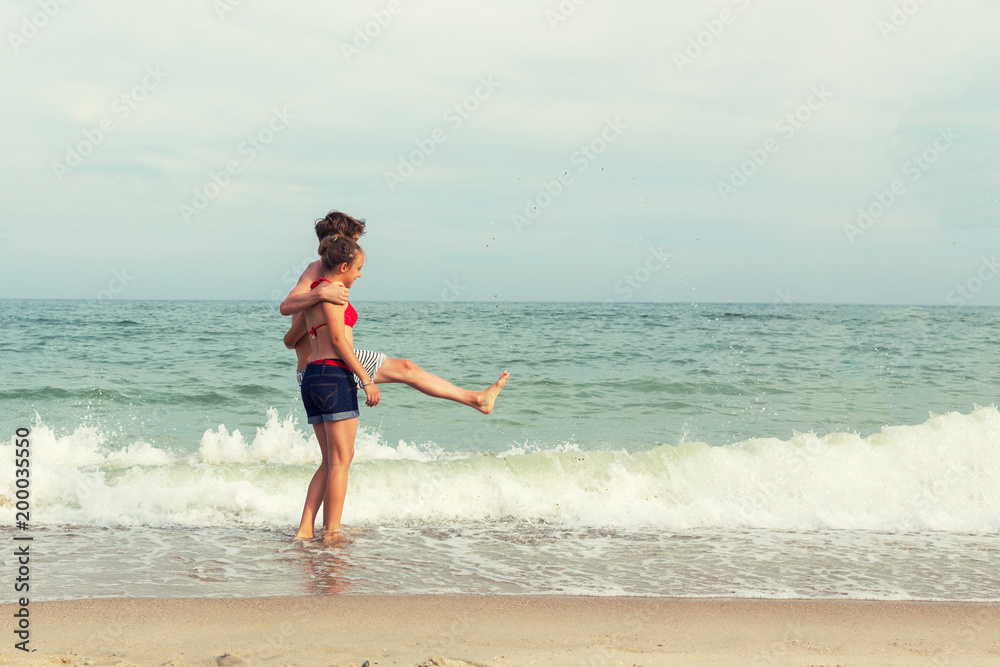 Two teenagers: a girl and a boy with blond hair, dressed in a swimsuit are walking on a sea beach. Copy space.